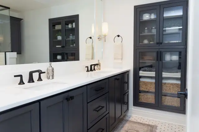 Condo bathroom renovation in Madison, WI with a black vanity and glass-front linen cabinet, white quartz top and matte black faucets