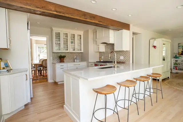 Kitchen remodeled with a garage addition in Madison, WI, with a long white peninsula, wood ceiling beam and wood-seat stools