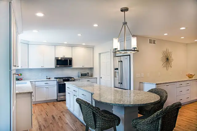 Kitchen remodel in Verona, WI with white cabinets, a granite-topped island with curved seating and a lantern pendant
