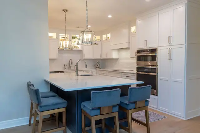 Madison, WI condo kitchen remodel with white shaker cabinets, glass-front uppers, a navy peninsula and blue upholstered stools